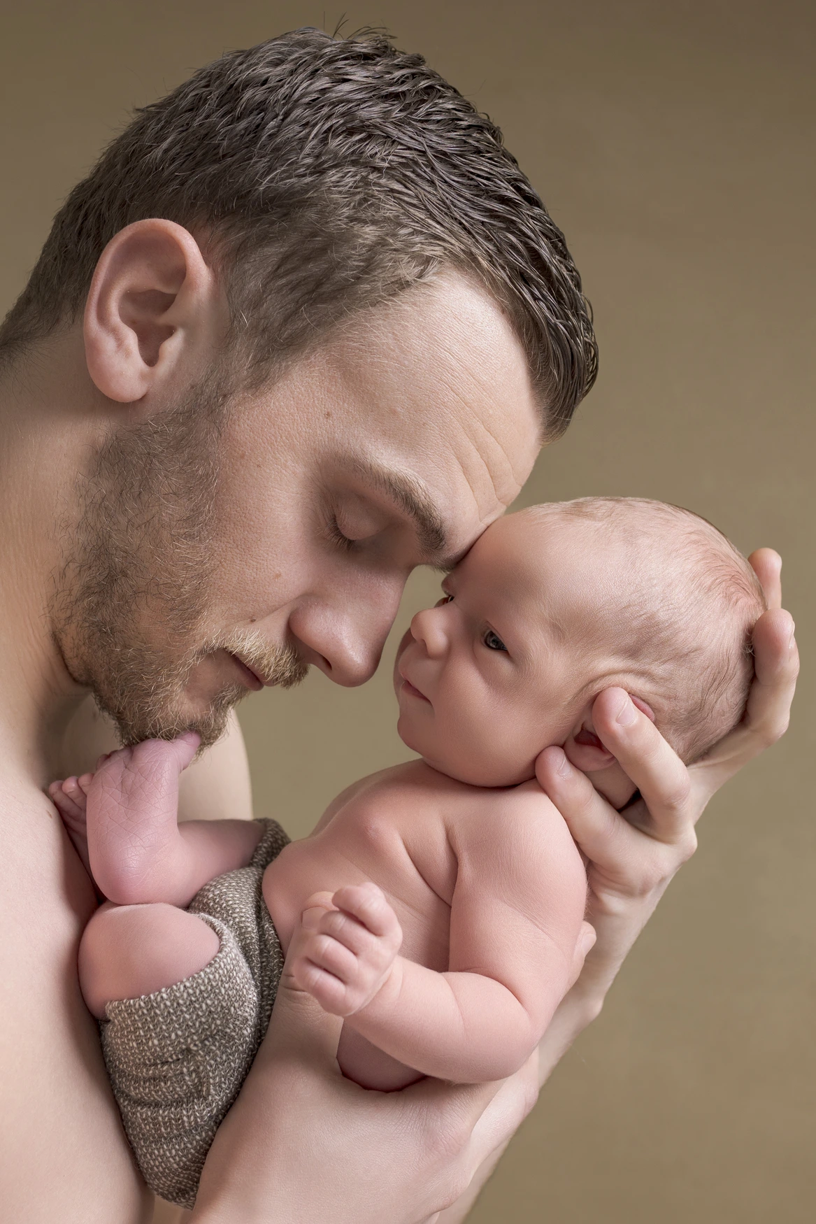 Photographie de naissance, la maman tient dans ses bras son bébé et lui fait un bisou sur le front
