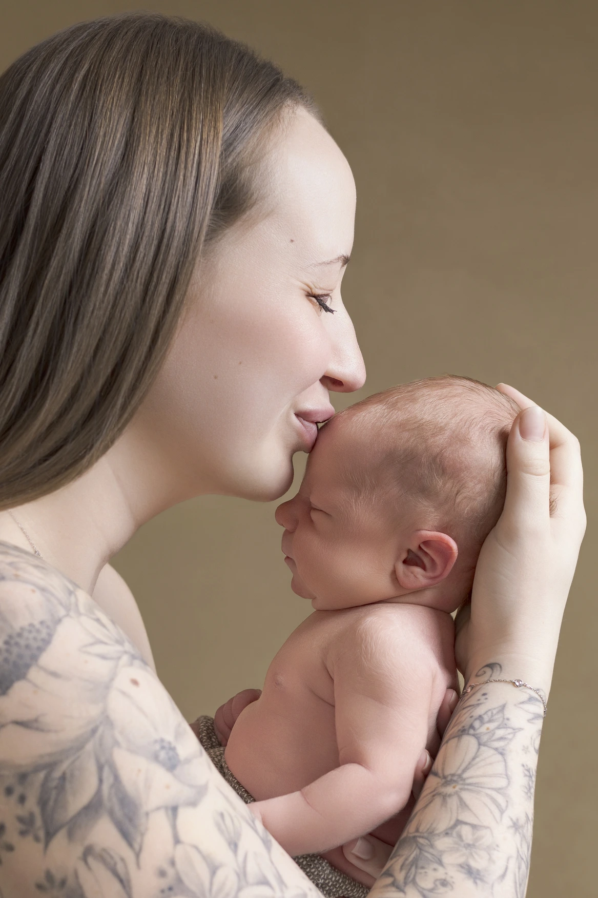 Photographie de naissance, la maman tient dans ses bras son bébé et lui fait un bisou sur le front
