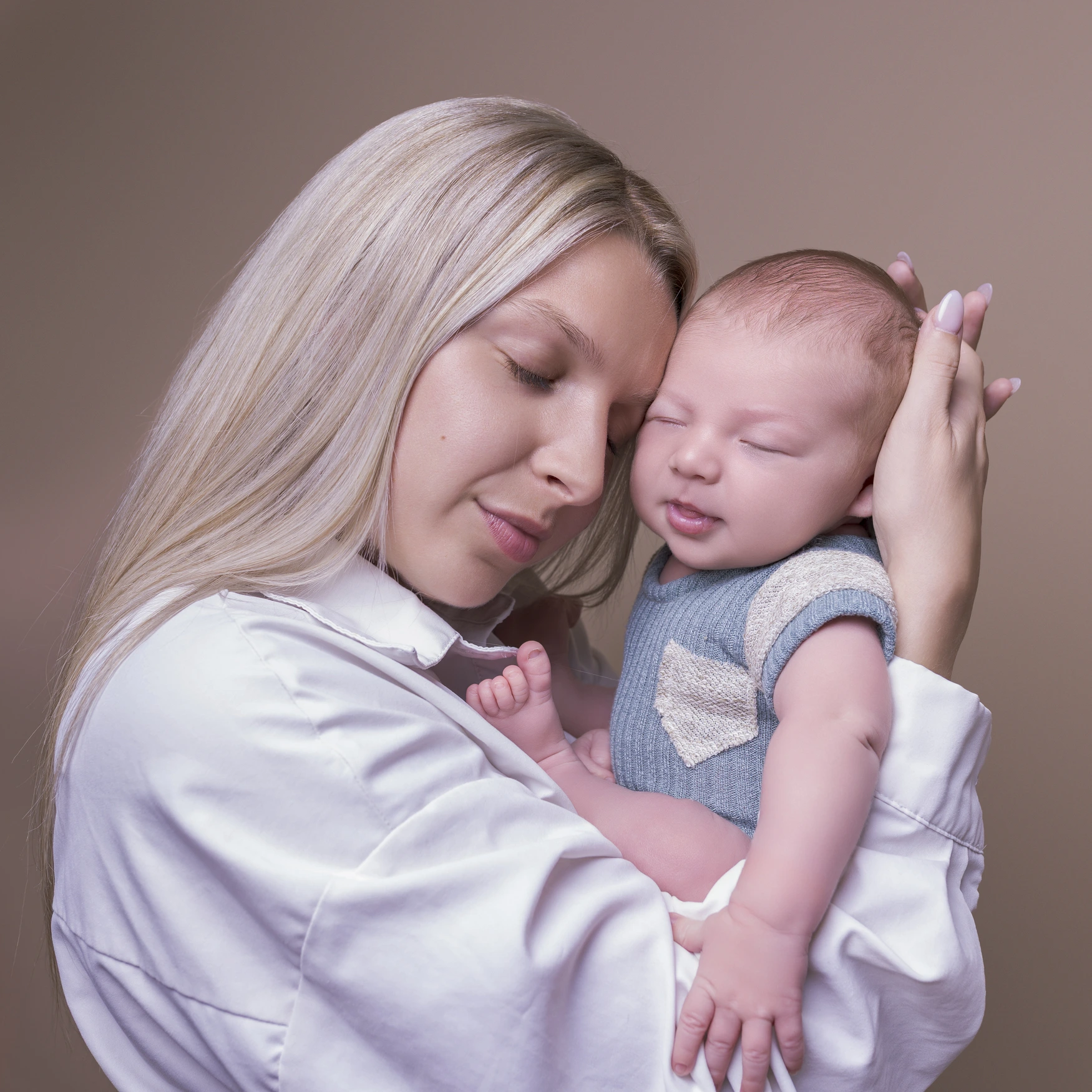 Photographie de naissance, la maman tient dans ses bras son bébé et lui fait un bisou sur le front